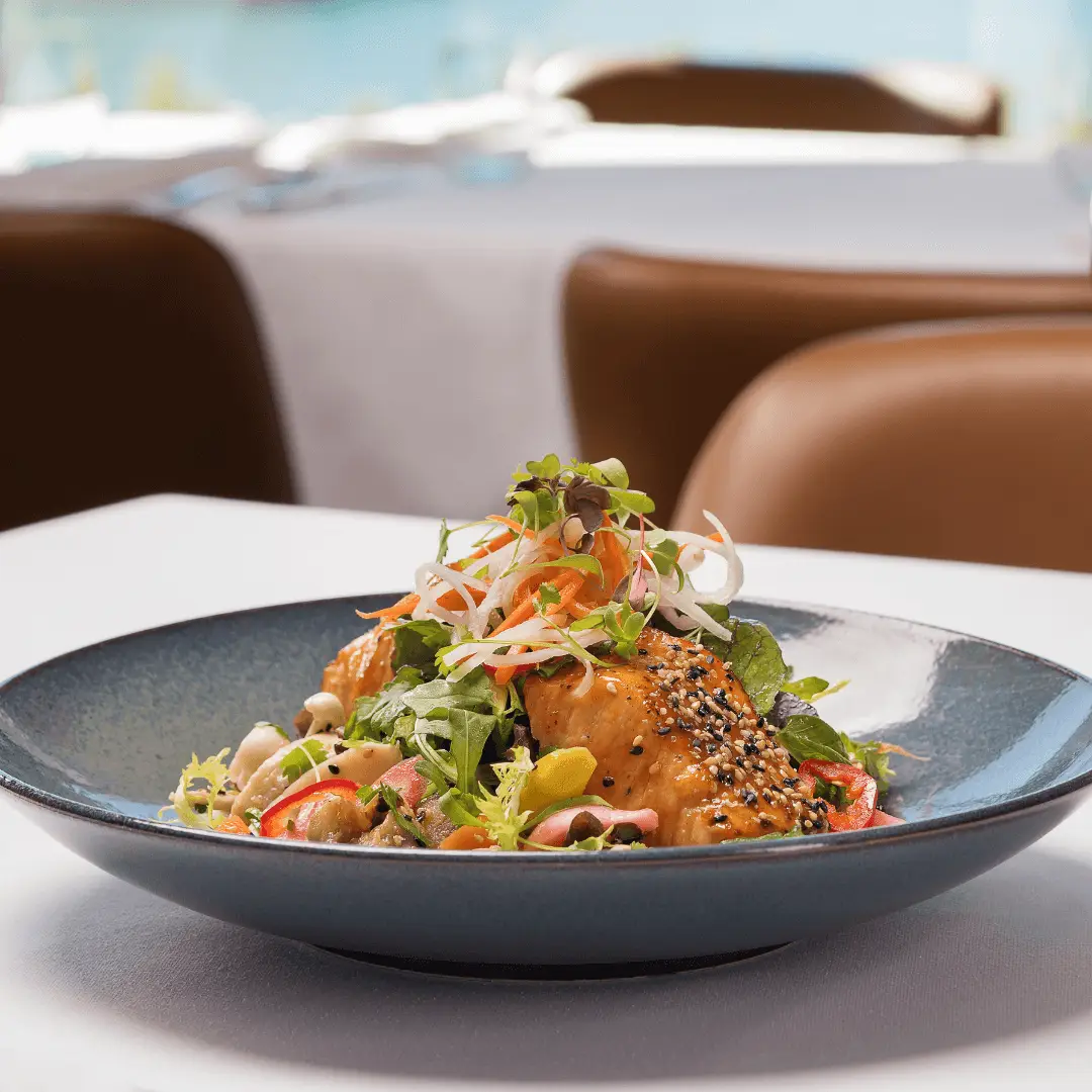 Closeup of a bowl with a miso glazed salmon on a bed of fresh greens.