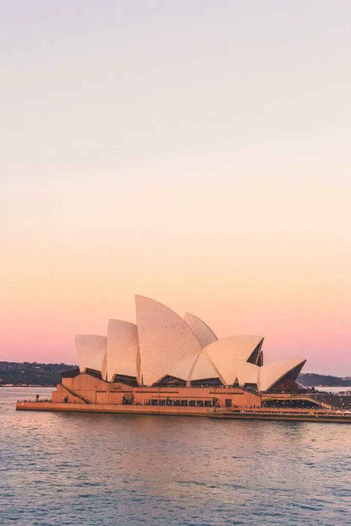 Photo of the Sydney Opera House set against a pink and yellow pastel sky.