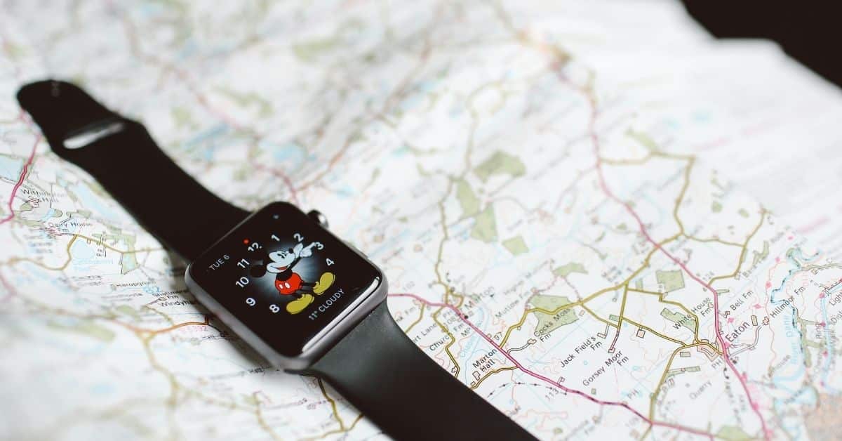 Closeup of a watch with Mickey Mouse on the face resting on a map..