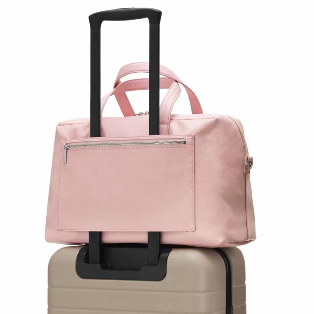 Closeup of a hardshell carry on suitcase with a tote bag slid over the luggage handle.