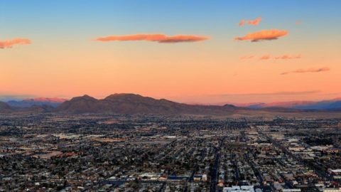 Panoramic aerial view of the sprawling metro Las Vegas area with mountains and sunset in the background.