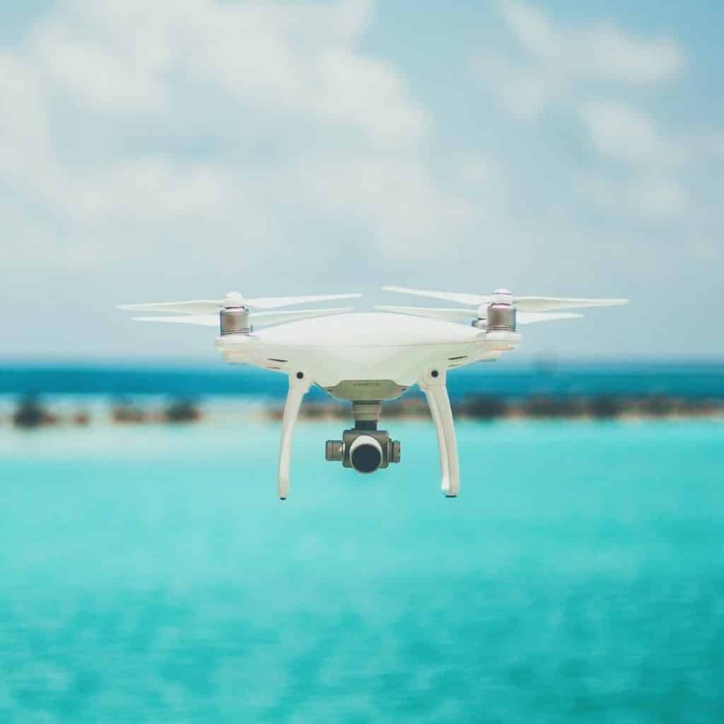 Closeup of a white photography drone hovering over turquoise water.