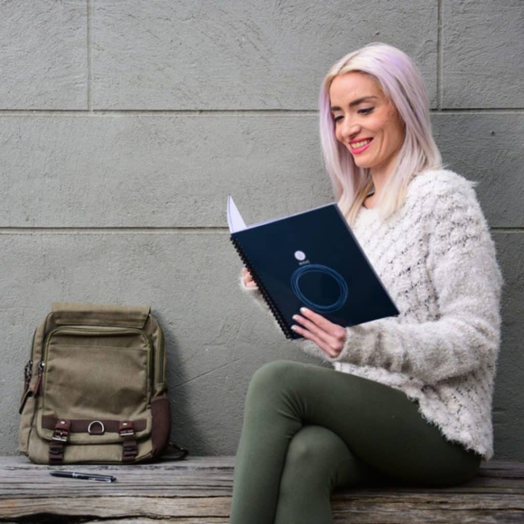 Photo of a woman sitting on a bench, browsing through a Rocketbook notebook.