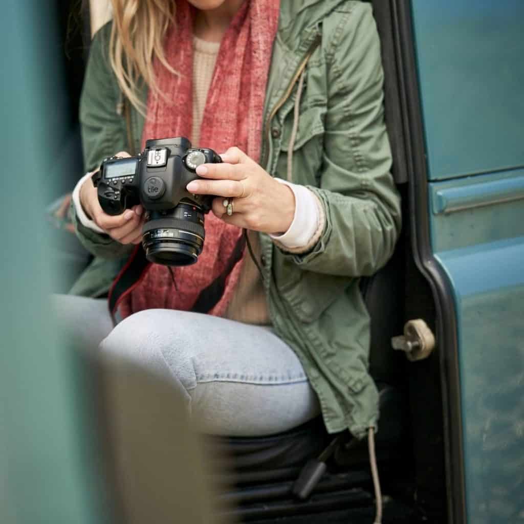 Closeup of a woman holding a professional camera with a Tile Sticker on it.