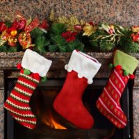 Closeup of a fireplace with an evergreen bough on the mantle and 3 Christmas stockings hanging.
