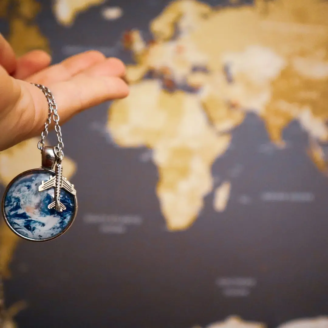 Closeup of a person holding a silver necklace chain with a silver plane charm and a globe-like charm.