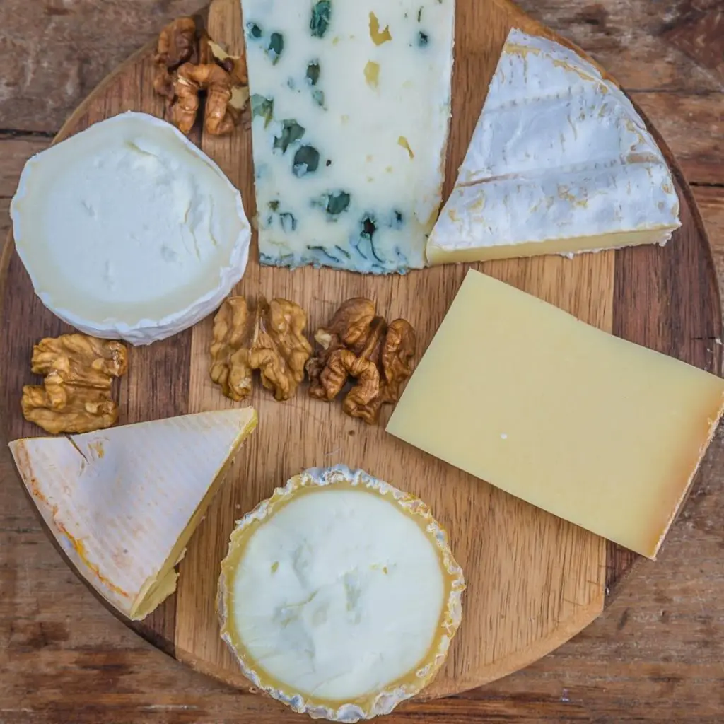 closeup of a round wooden board with an assortment of French cheeses and walnuts.