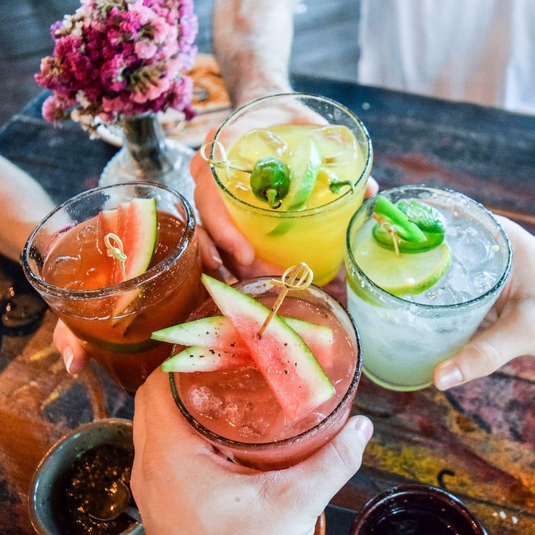 Closeup of 4 people holding colorful margarita cocktails.