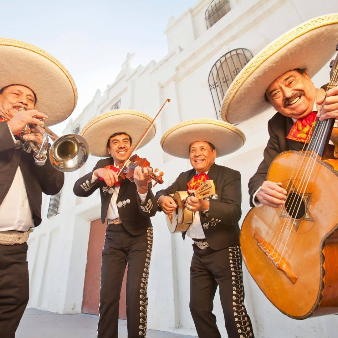 Photo of 4 men dressed in traditional Mariachi costumes, playin instruments.