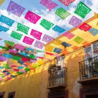 Photo of a yellow building with colorful flags strung up over the street.