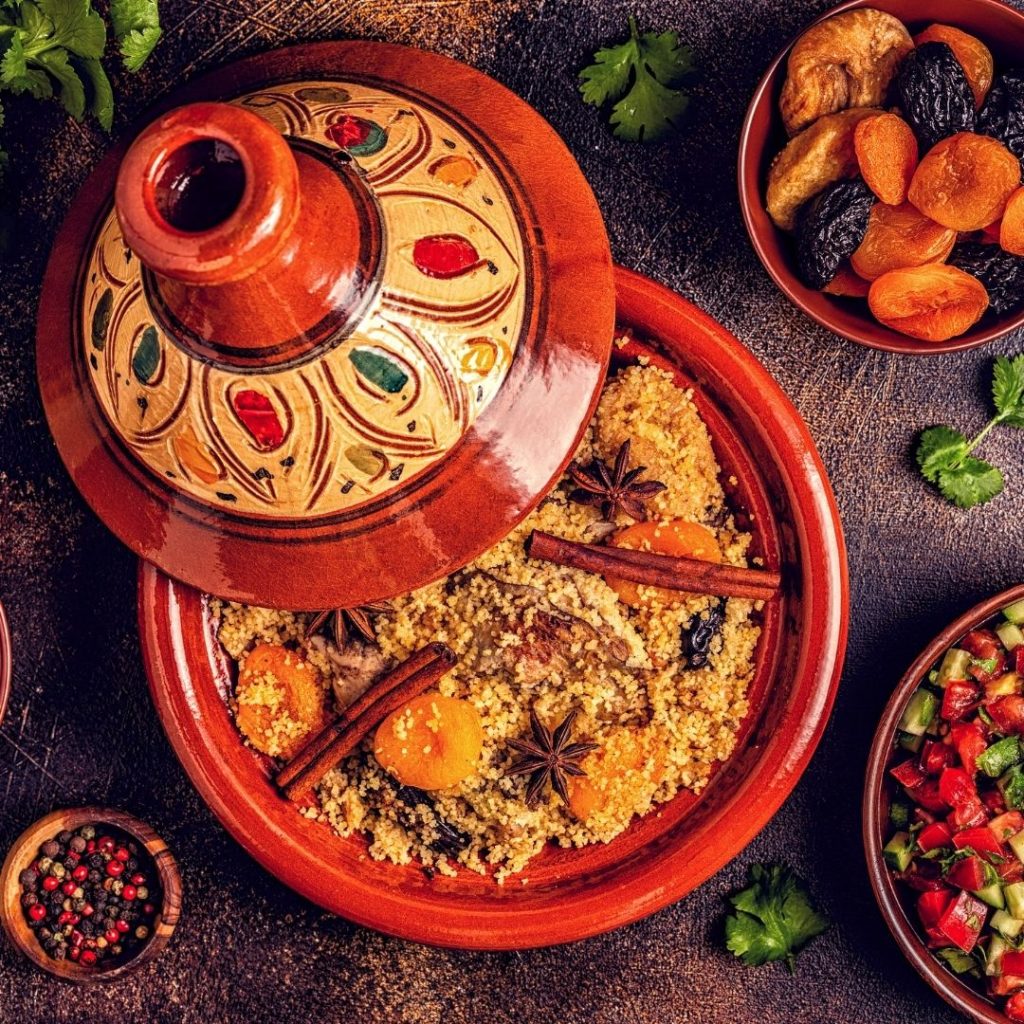 Closeup of Moroccan tagine in traditional pottery with a bowl of dried fruit and spices nearby.