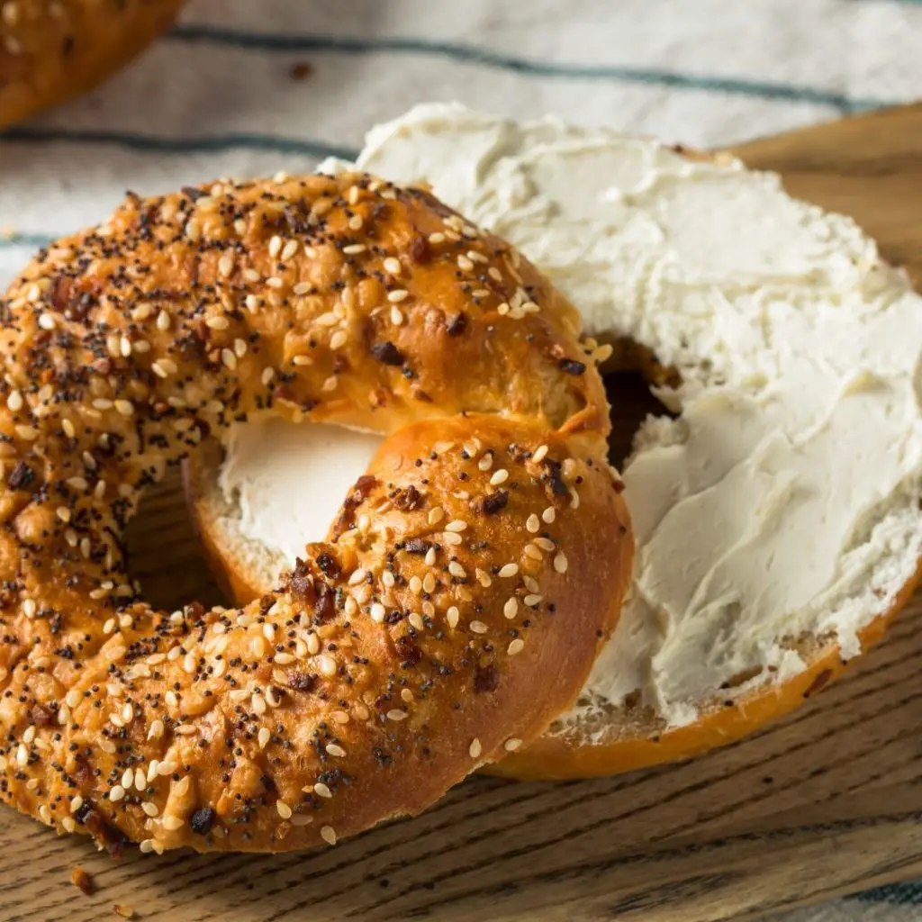 Closeup of an everything bagel, sliced, with plain cream cheese smeared on the bottom half.