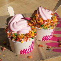 Closeup of 2 cups of pink soft serve ice cream from Milk with Fruity Pebbles cereal sprinkled on top.