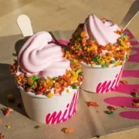 Closeup of 2 cups of pink soft serve ice cream from Milk with Fruity Pebbles cereal sprinkled on top.