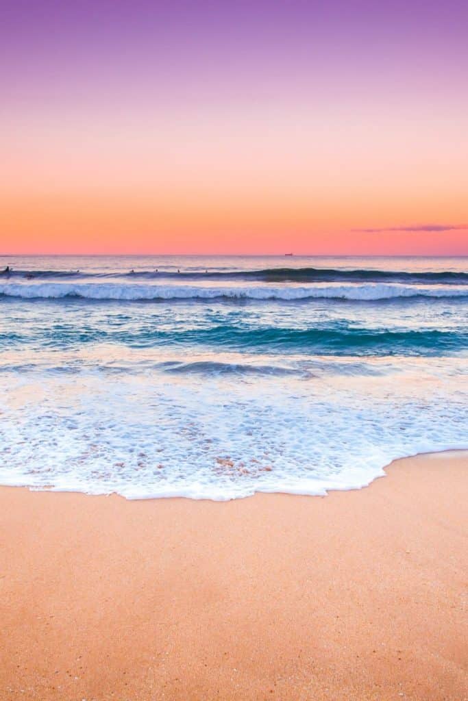 Photo of a beach at sunset with purple, pink, and orange sky.
