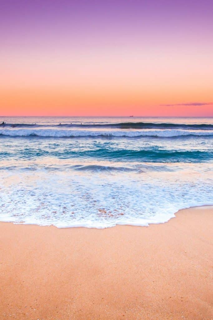 Photo of a beach at sunset with purple, pink, and orange sky.