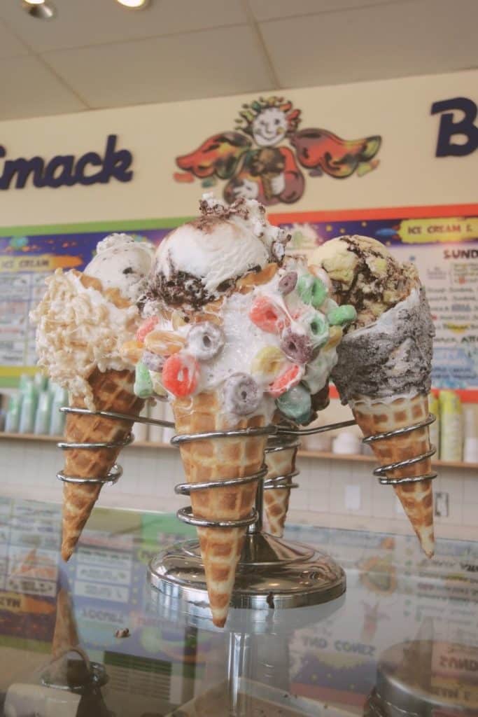 Closeup of a stand holding several candy coated ice cream cones with ice cream in them. A sign in the background says "Emack & Bolios."