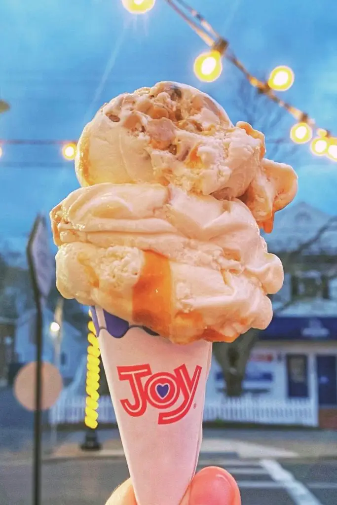 Closeup of an ice cream cone with caramel ribbons in the ice cream and a street in Cape Cod in the background.