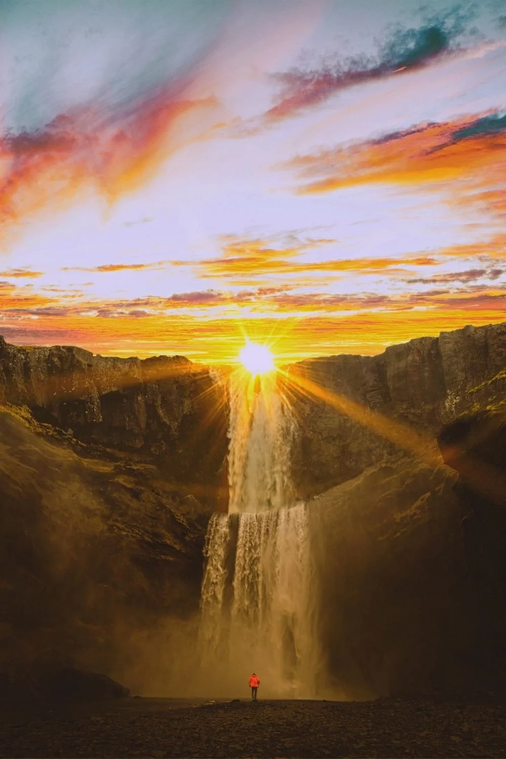 Photo of the sun setting behind giant mountains with a waterfall.