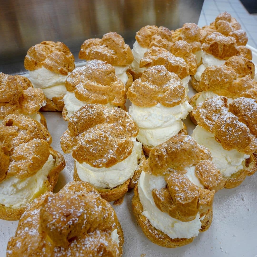 Closeup of a tray full of cream puffs topped with a dusting of powdered sugar.