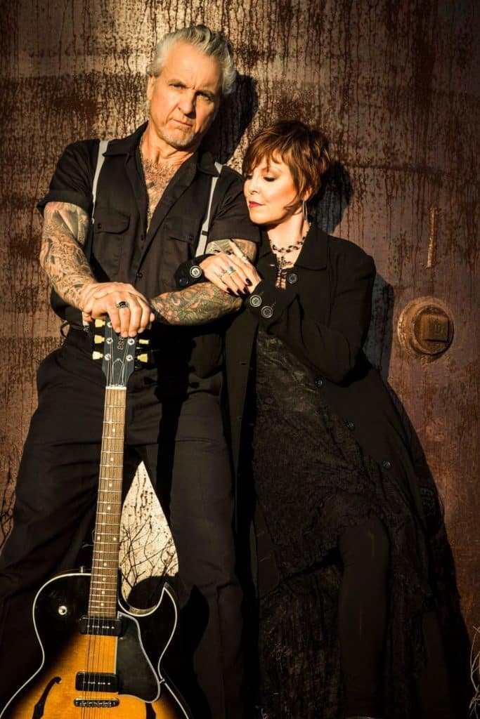 Press photo of musicians Pat Benatar and Neil Giraldo posing with a guitar.