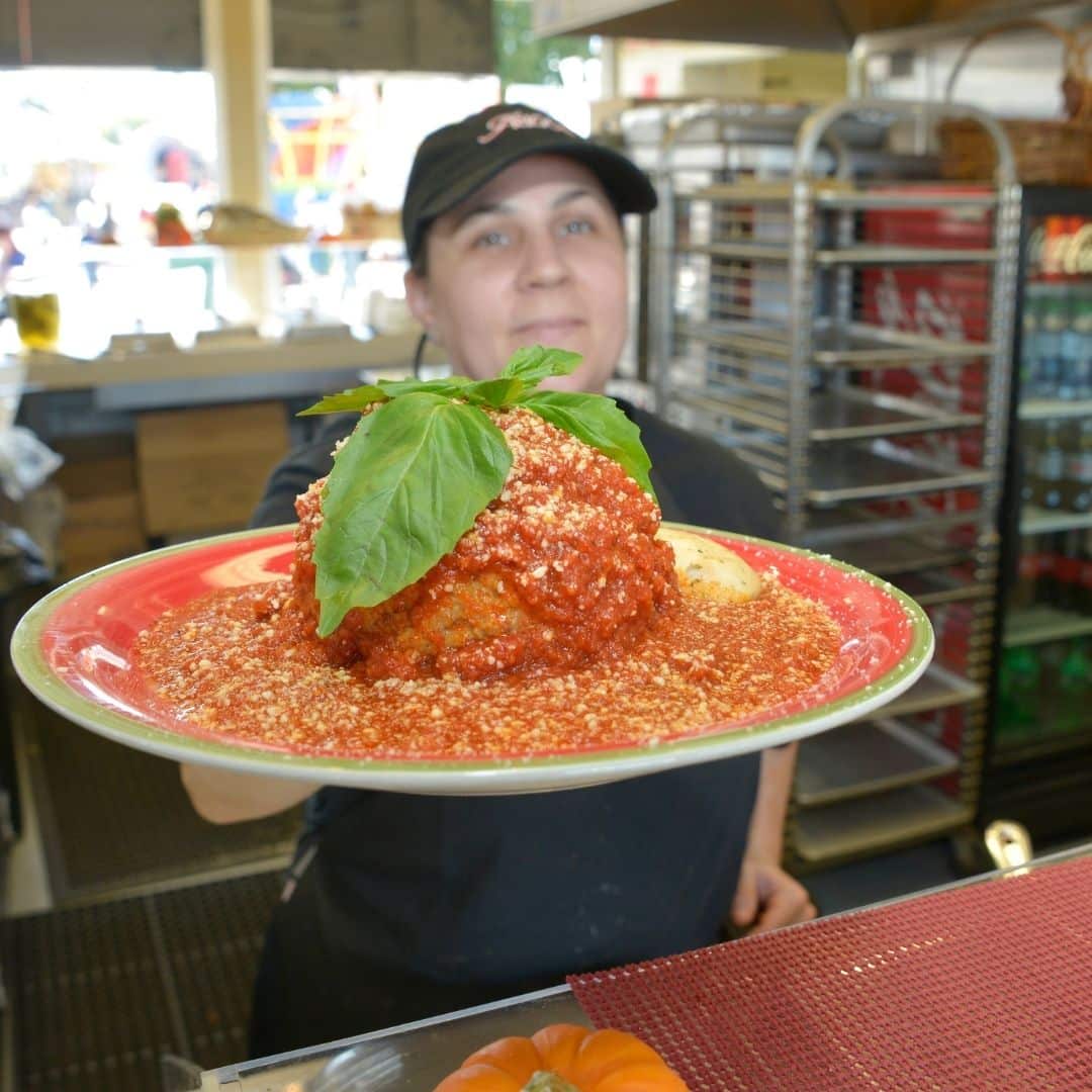 Closeup of a person holding a plate with a giant 1 pound meatball covered in tomato sauce.
