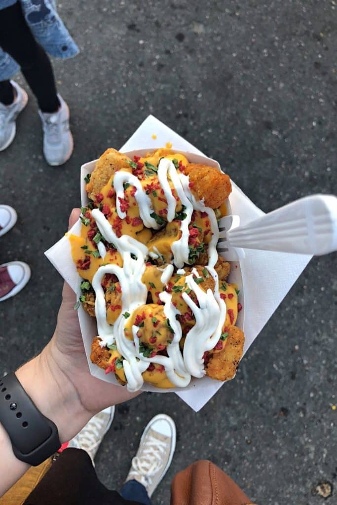 Top down photo of a basket full of tater tots topped with cheese sauce, sour cream, bacon, and chives.