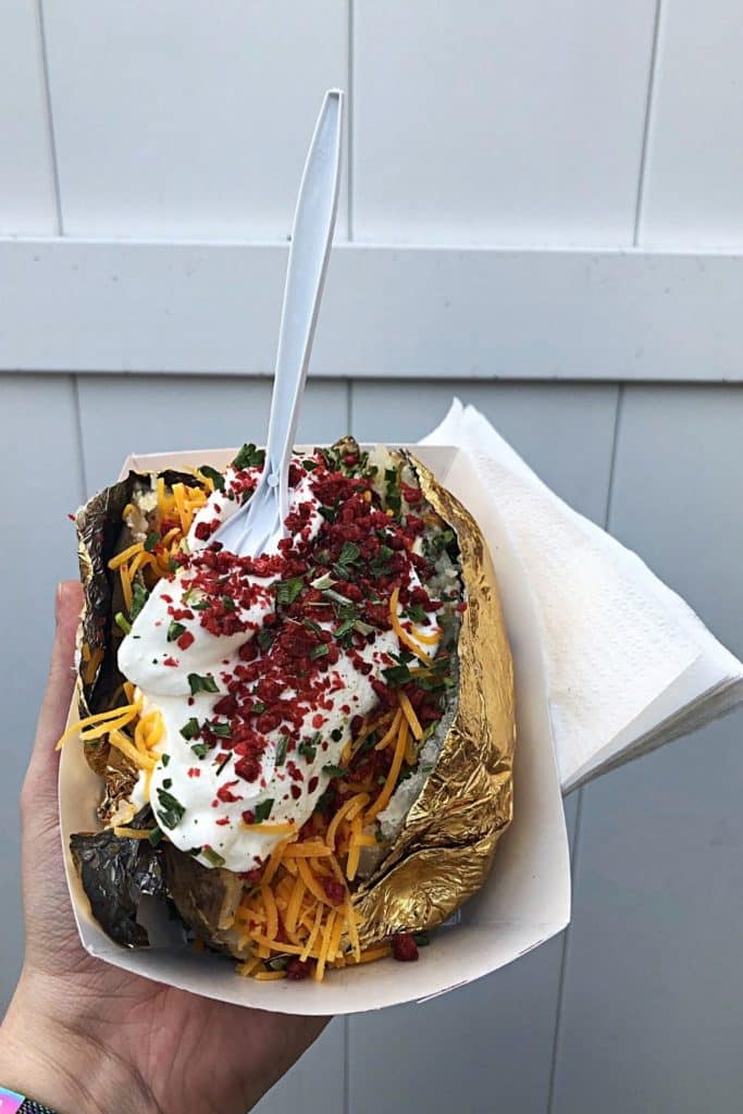 Closeup of a massive Maine baked potato topped with shredded cheddar cheese, sour cream, bacon, and chives.