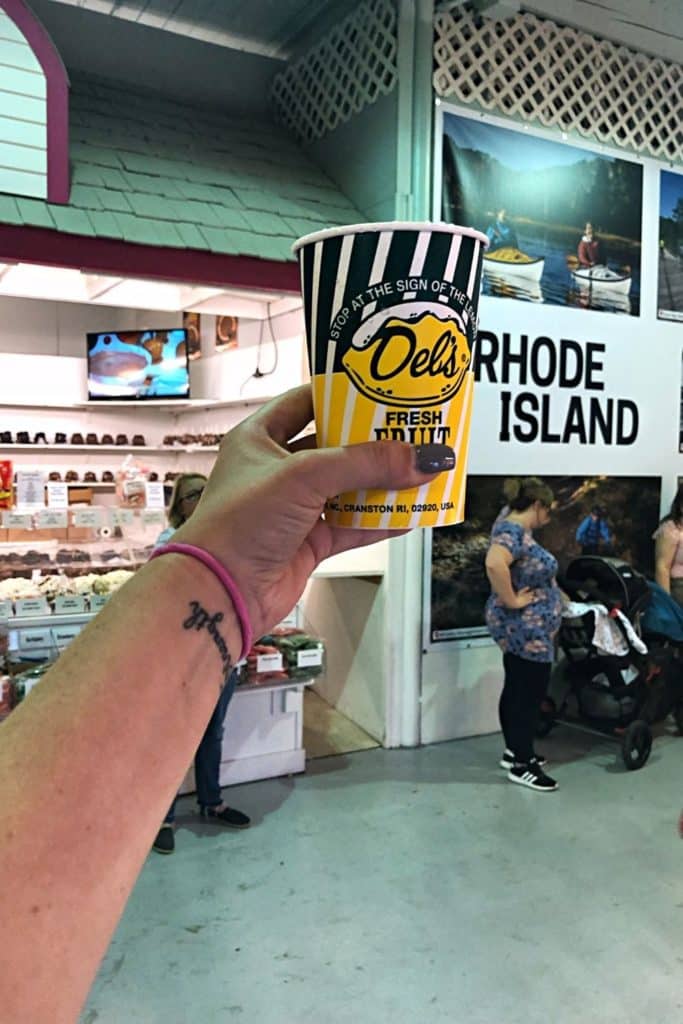 Photo of a person holding up a cup of Del's fresh lemonade inside the Rhode Island building at The Big E Avenue of States.