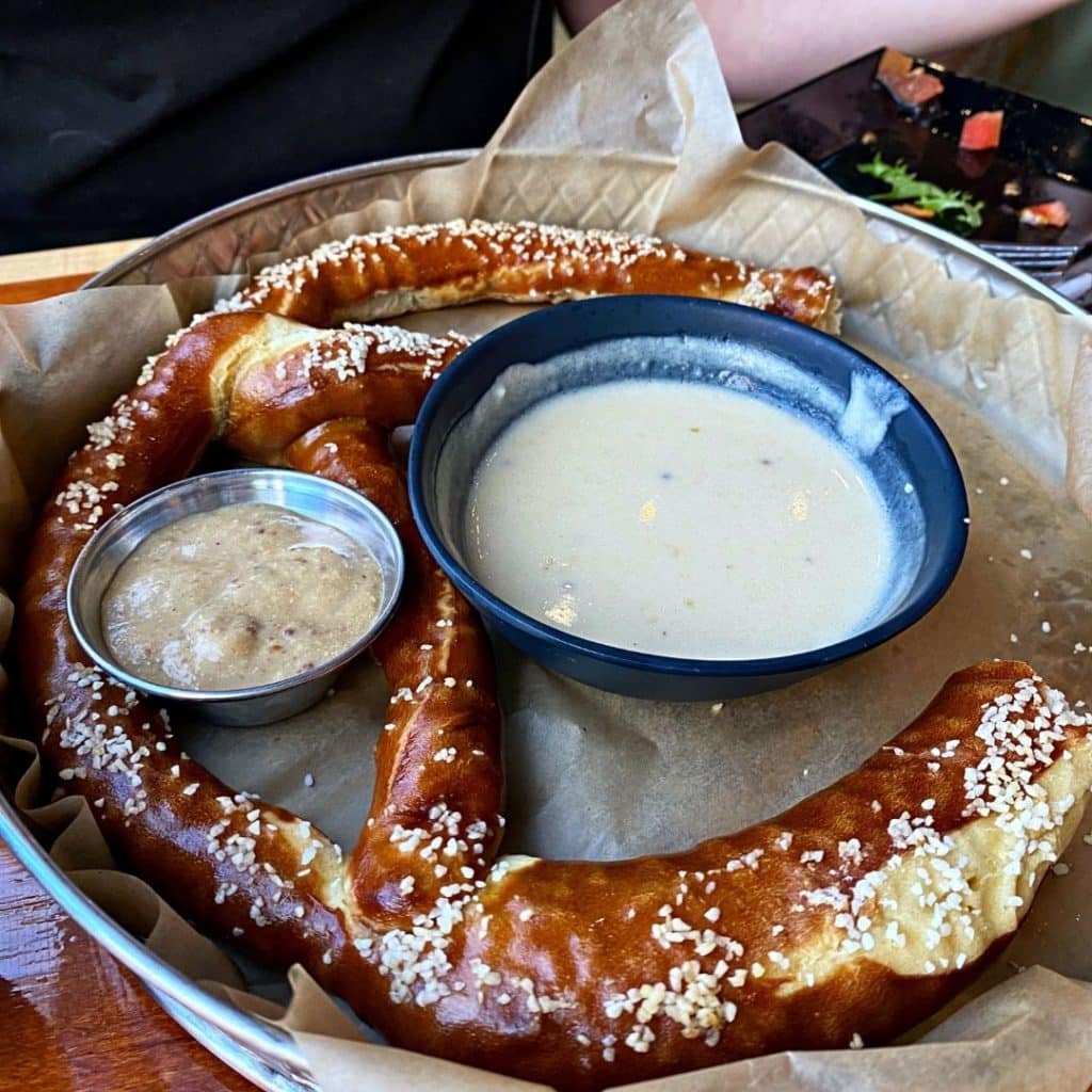 Closeup of a giant baked pretzel with a cup of German mustard and a bowl of beer cheese.