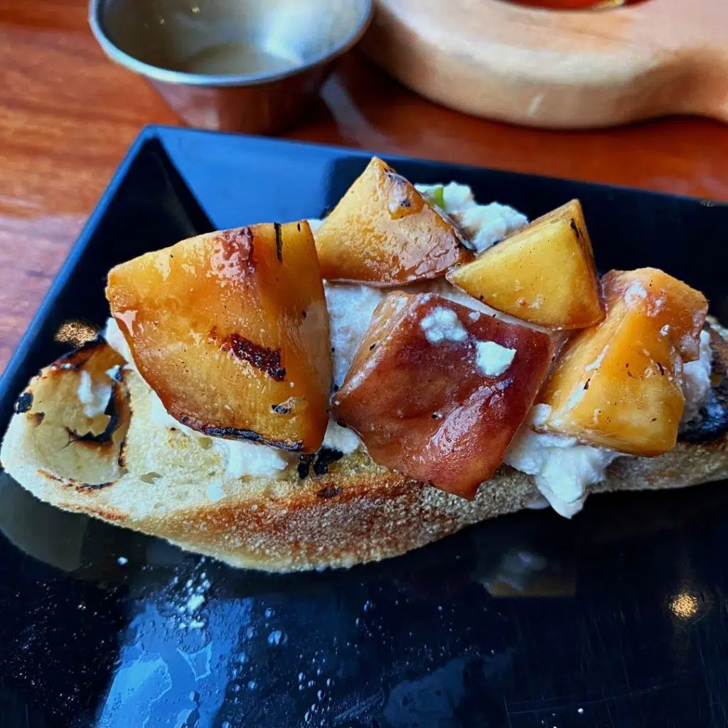 Closeup of toast with smoked burrata mozzarella cheese and grilled peaches on top.