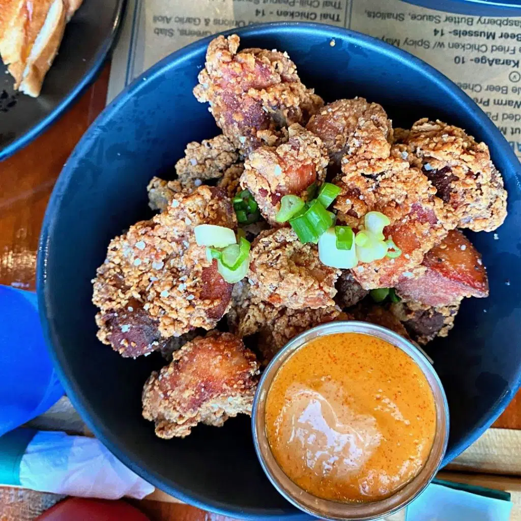 Flat lay view of a bowl of Japanese fried chicken thigh bites with a spicy sauce in a cup.