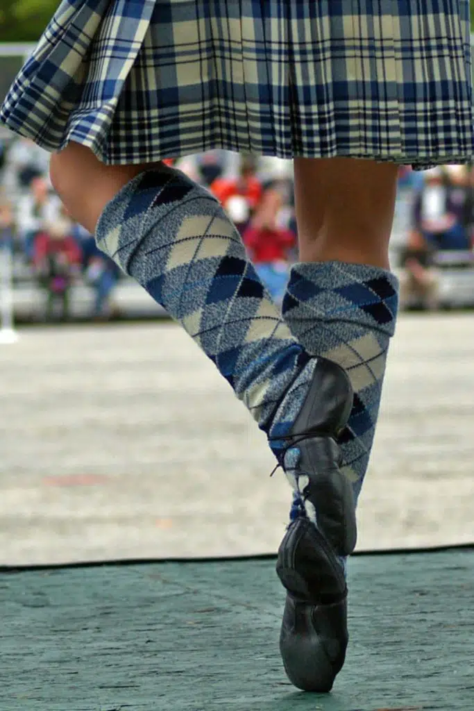 Closeup from behind of a woman performing Scottish folk dancing while dressed in blue plaid and argyle.