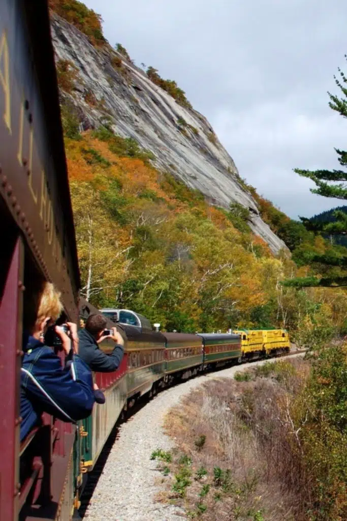 Photo of a train rounding a curve with passengers leaning out the window to capture photos of the Fall foliage.