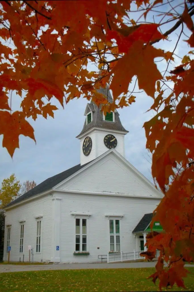 Photo of a white church in Sugar Hill, NH with Autumn leaves framing the photo.