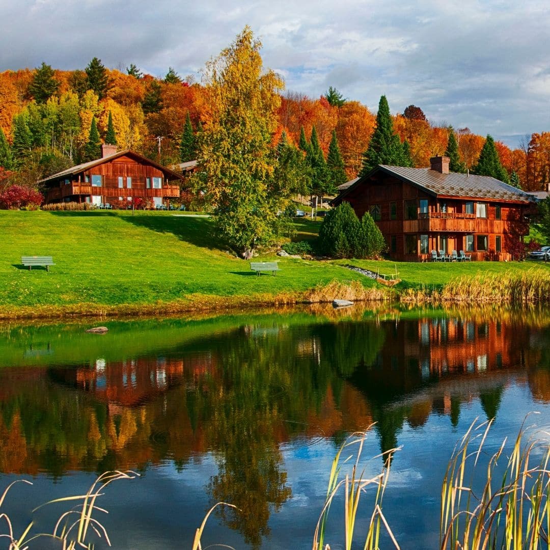 Landscape view of the Trapp Family Lodge with a pond in the foreground, and several lodges and cabins set against Fall foliage in the background.
