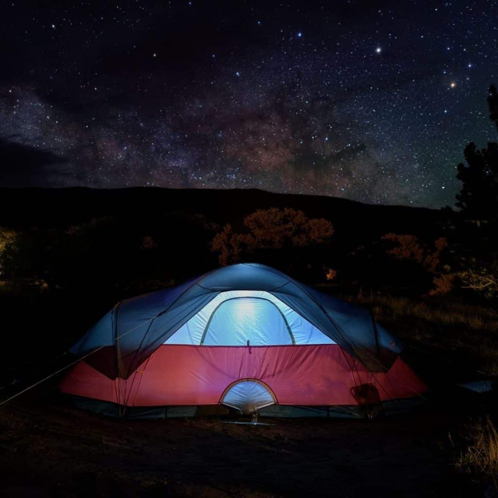 Photo of a tent at night with lots of stars in the sky.