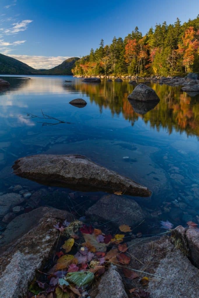 Photo of Jordan Pond in Acadia National Park with Fall foliage along the shore, reflecting in the pond.