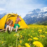 Photo of 5 kids hanging out in a tent in a field of dandelions with mountains in the background.