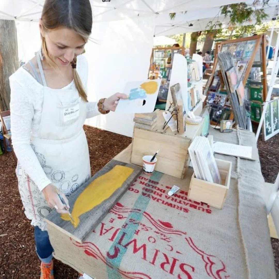 Photo of a woman painting a wooden plank at the Freeport Fall Festival in Freeport, Maine.