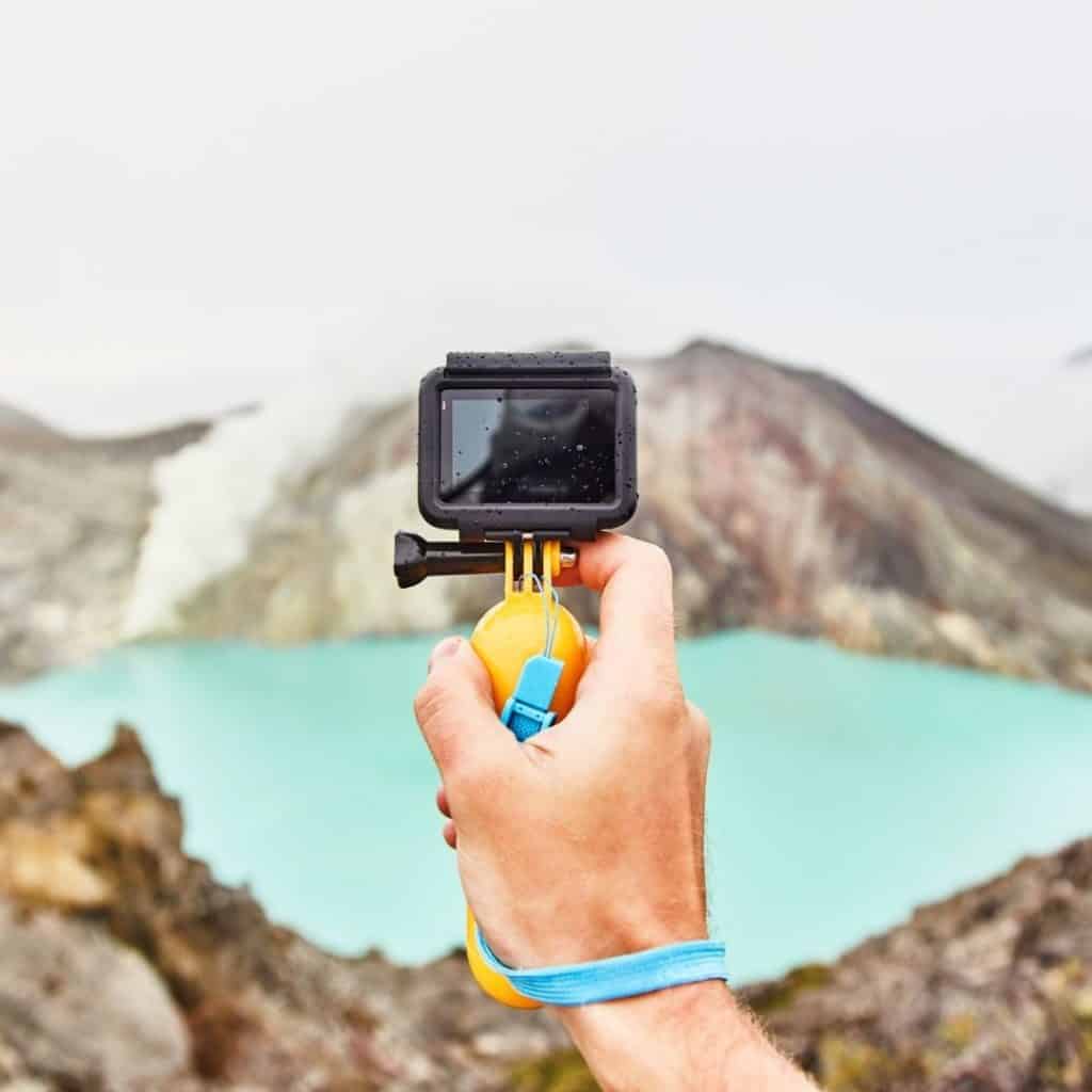 Closeup of a hand holding up a GoPro camera with mountains in the background.