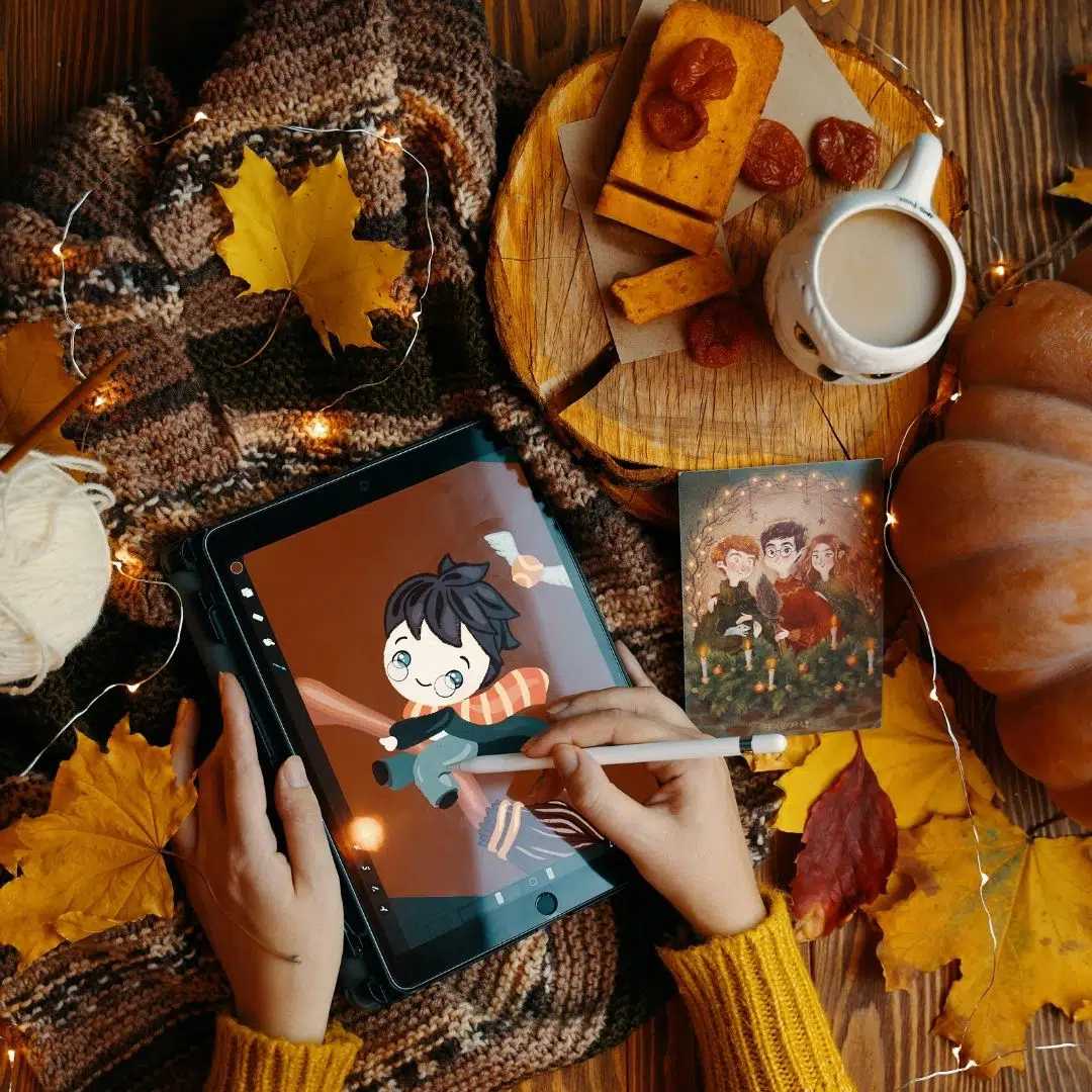 Top-down photo of a person drawing Harry Potter with Fall decor arranged on the table.