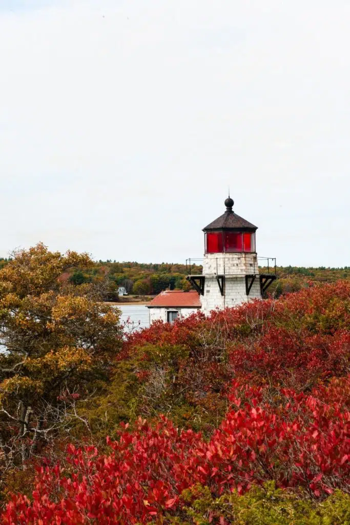 Photo of an old lighthouse with Fall foliage in the landscape.