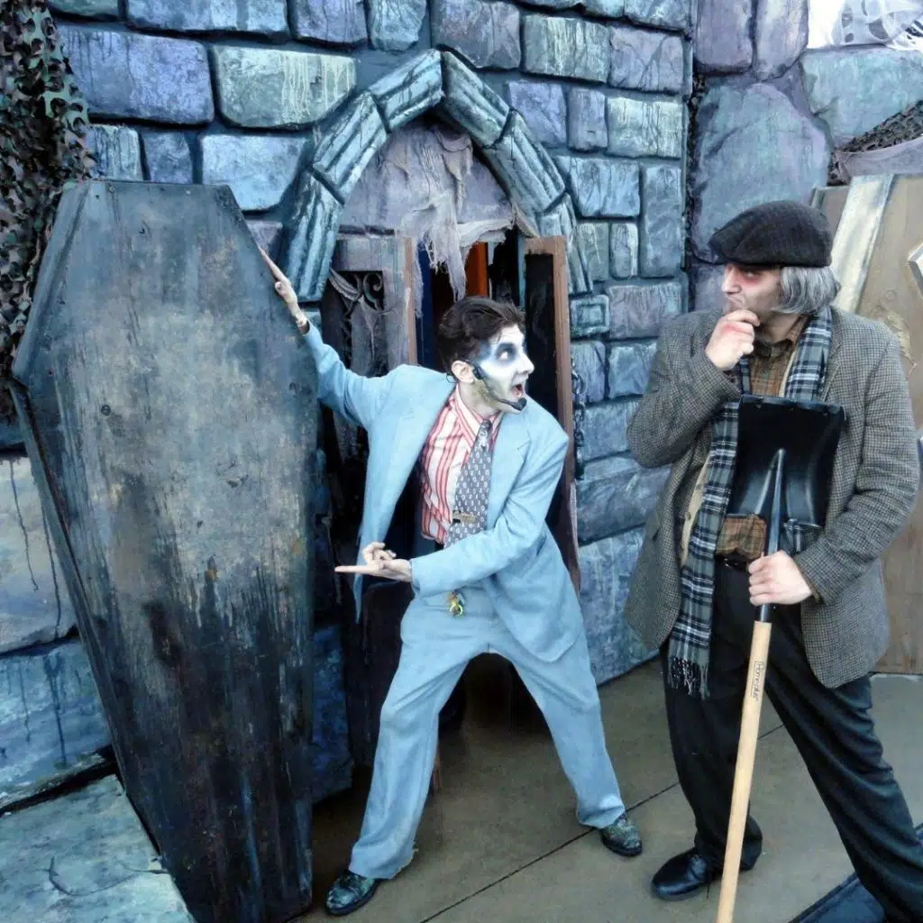 Photo of 2 actors dressed as ghosts, acting out a scene with a coffin and a shovel.