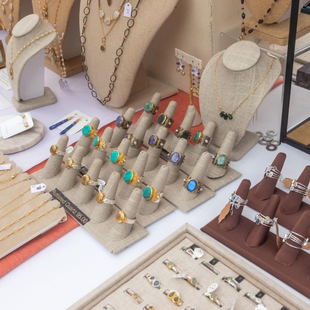 Closeup of a table with many different handmade jewelry displays, such as rings and necklaces.