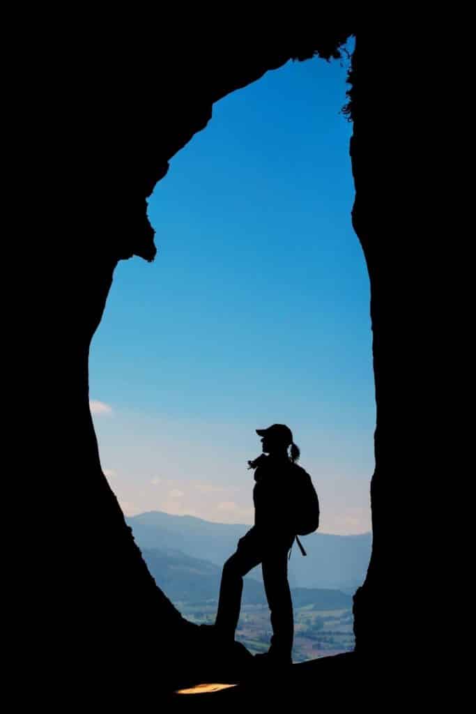 Photo of a silhouette of a woman with a backpack standing in an opening between rocks.