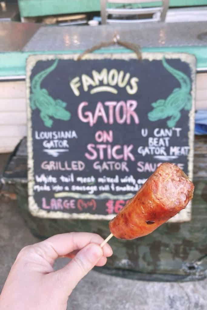 Closeup of alligator sausage with a "gator on a stick" sign in the background.