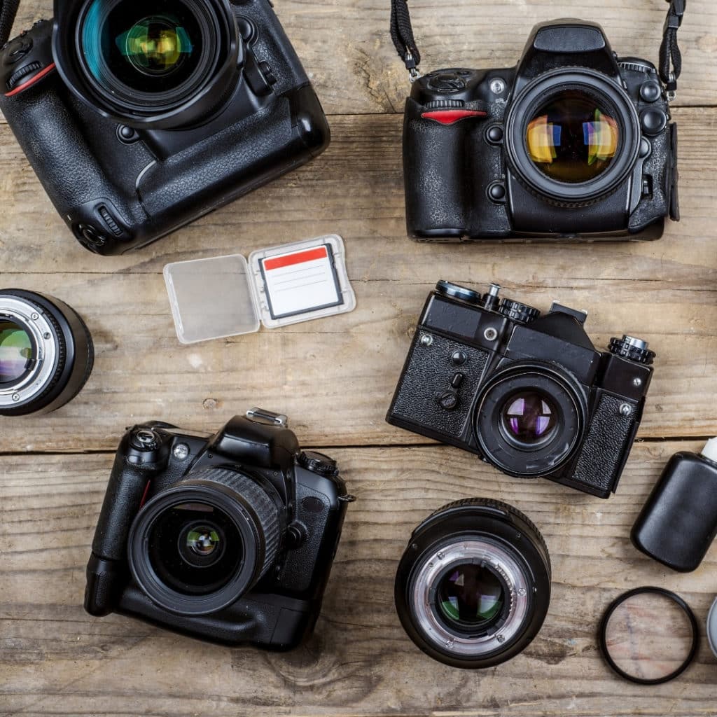 Flat lay photo of cameras and lenses on a wooden surface.