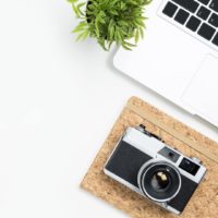 Photo of a white desk with a laptop, notebook, and camera.