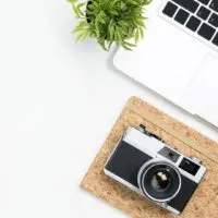 Photo of a white desk with a laptop, notebook, and camera.